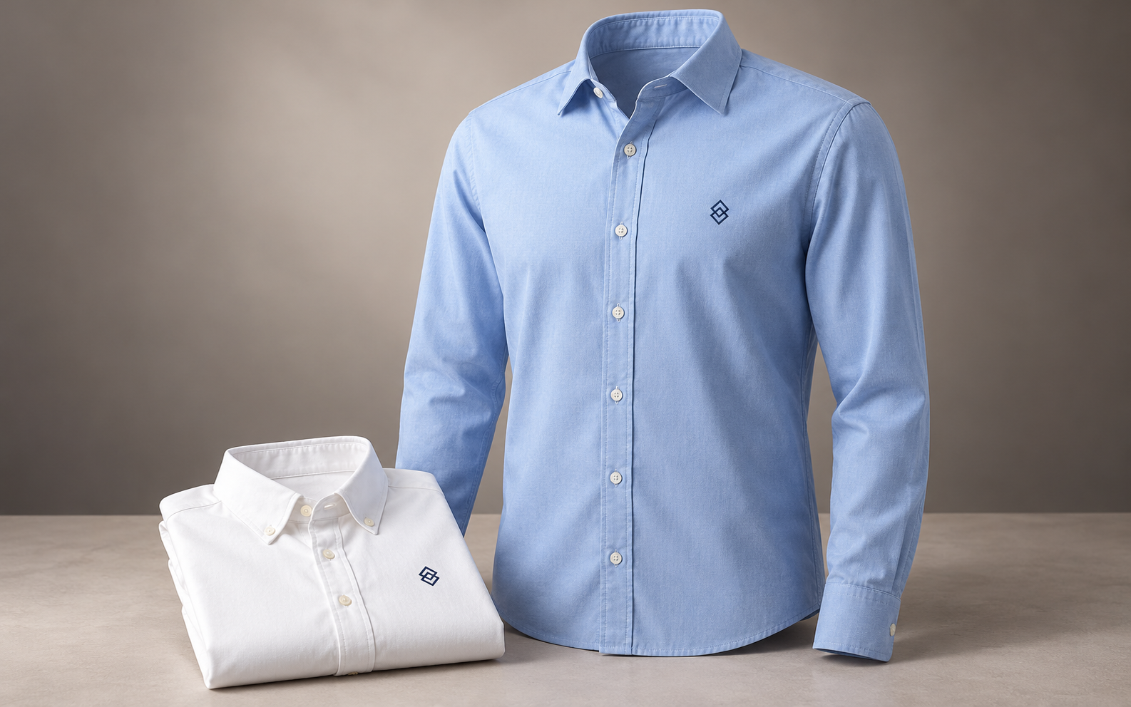 Camisa azul claro de botones con logotipo discreto junto a una camisa blanca doblada